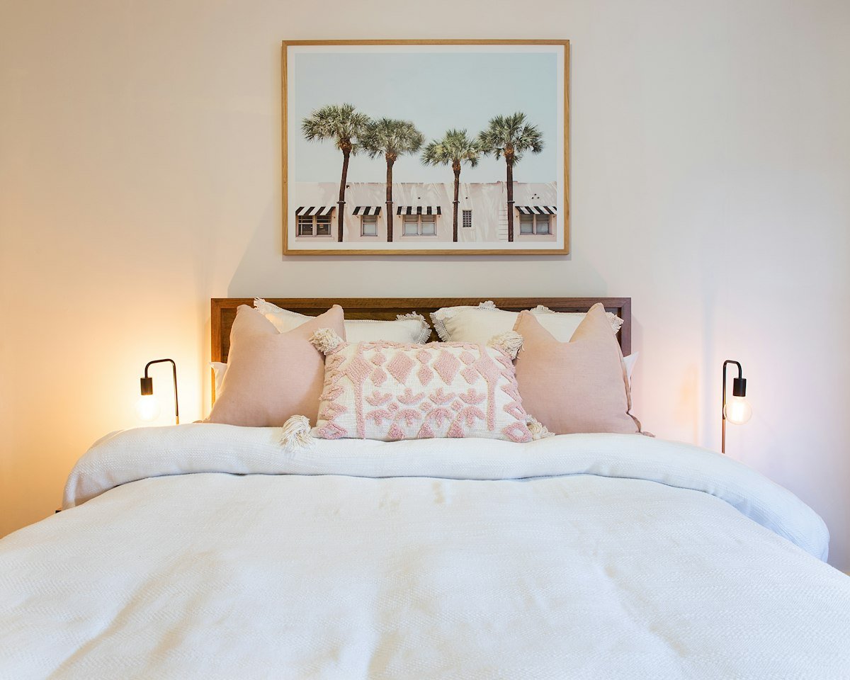 Chambre de location saisonnière au lit fait, linge blanc et coussins roses, prête pour les voyageurs